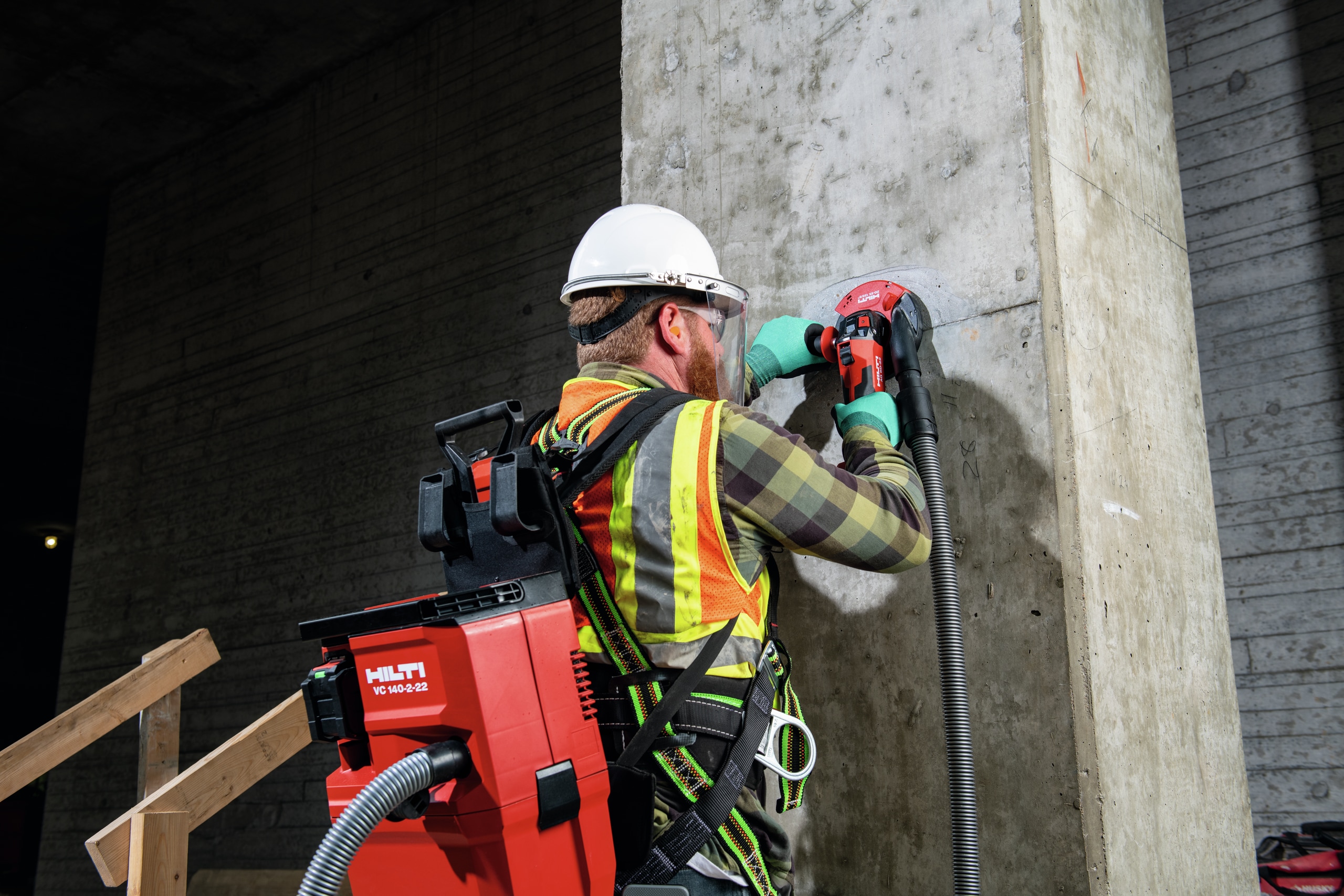 a worker grinding a concrete wall has a cordless vacuum cleaner on his back