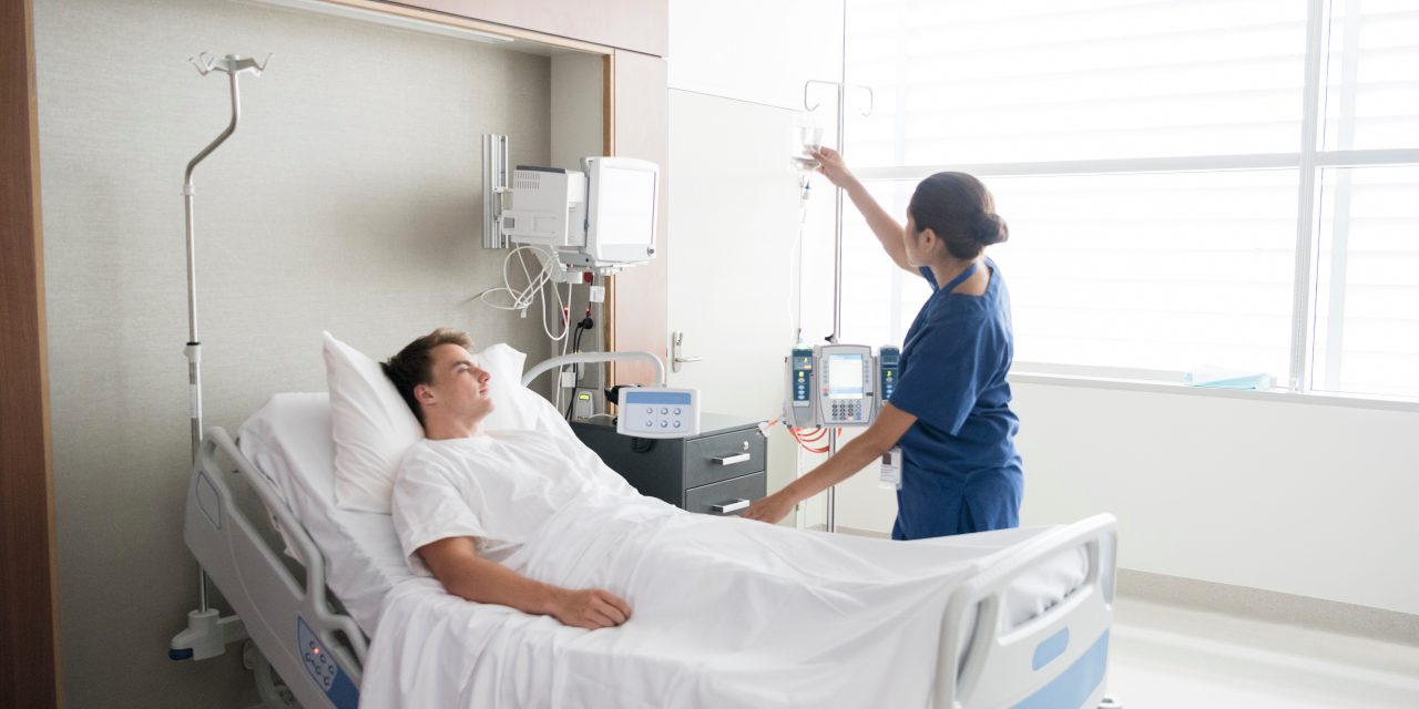 501709664 Young man in hospital being cared for by nurse. Medical professional looking after patient on hospital ward. Adjusting iv line, medication, care, bedside manner.